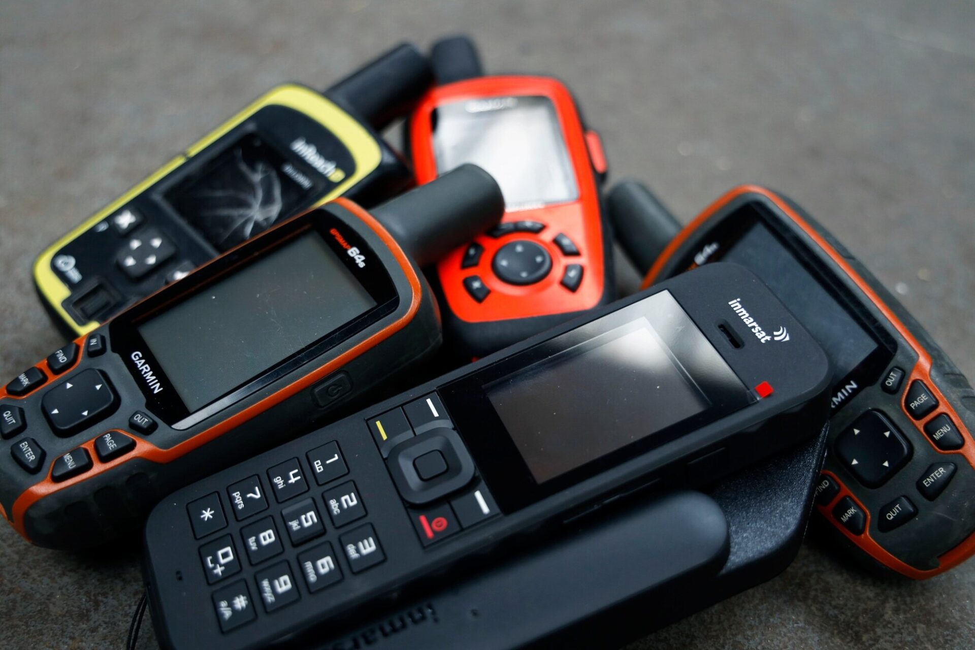 Modern GPS units including the Garmin InReach and a modern Inmarsat satellite phone.