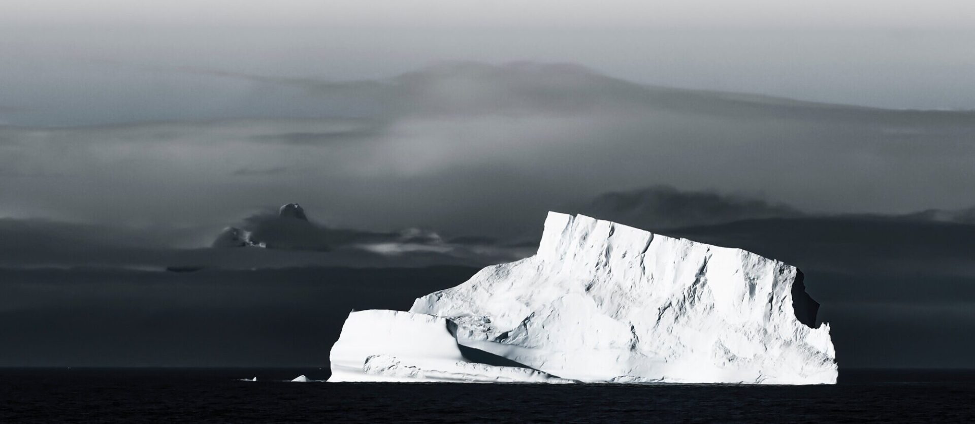 A massive iceberg drifts in front of a distant mountain range in the Antarctic Peninsula under the morning mist.