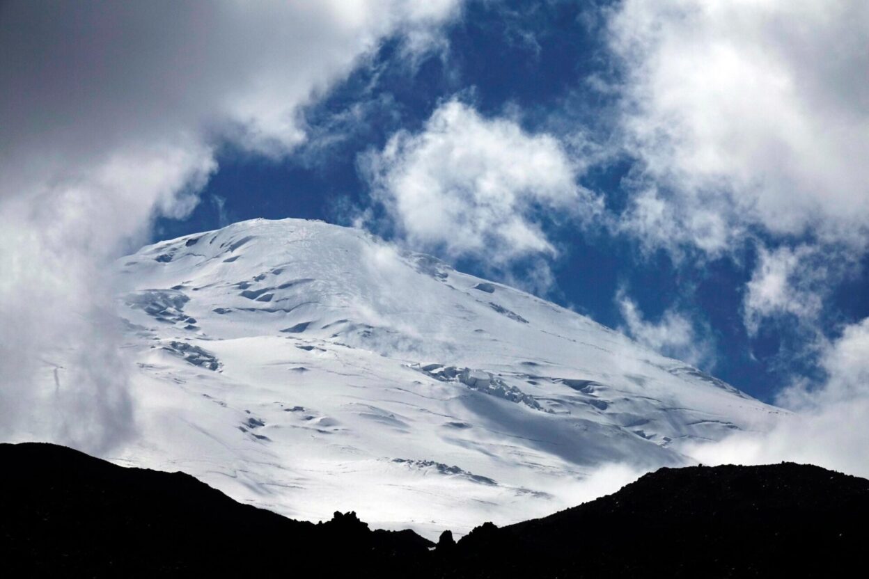 The higher west summit of Mount Elbrus appears through swirling afternoon cloud above high camp at North Hut. From here, it’s still 1900 metres to the top.