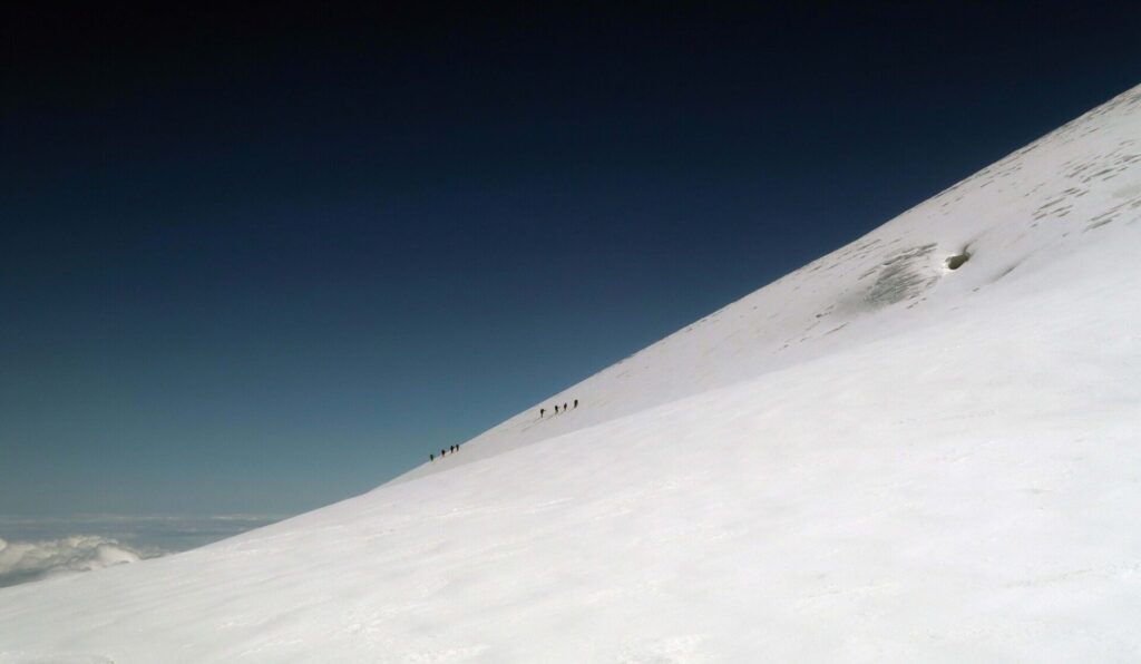 Two rope teams of four climbers moving steadily up the huge saddle-like feature between the east and the west summit of Elbrus.
