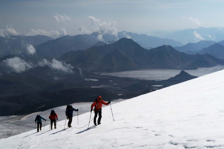 Four climbers roped together on the Bourbzalitchiran glacier, ascending towards the distinctive Lenz Rocks at 4500m. These rocks are a useful topographical reference on an otherwise vast and featureless mountain: a rest stop is normally made here during the ascent.