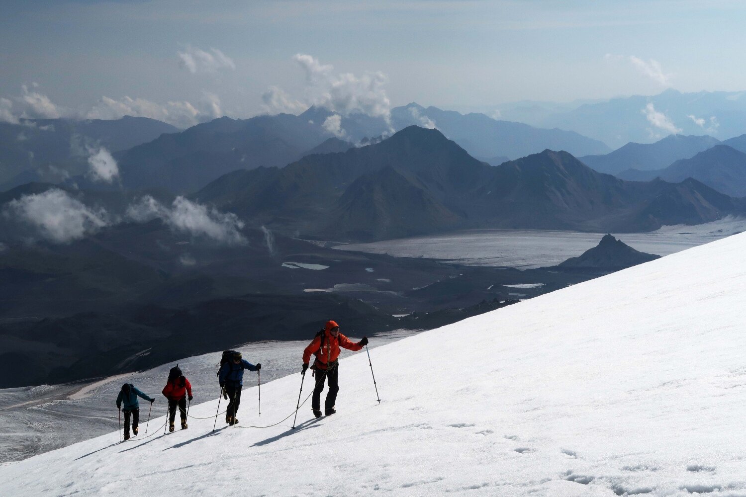 Four climbers roped together on the Bourbzalitchiran glacier, ascending towards the distinctive Lenz Rocks at 4500m. These rocks are a useful topographical reference on an otherwise vast and featureless mountain: a rest stop is normally made here during the ascent.