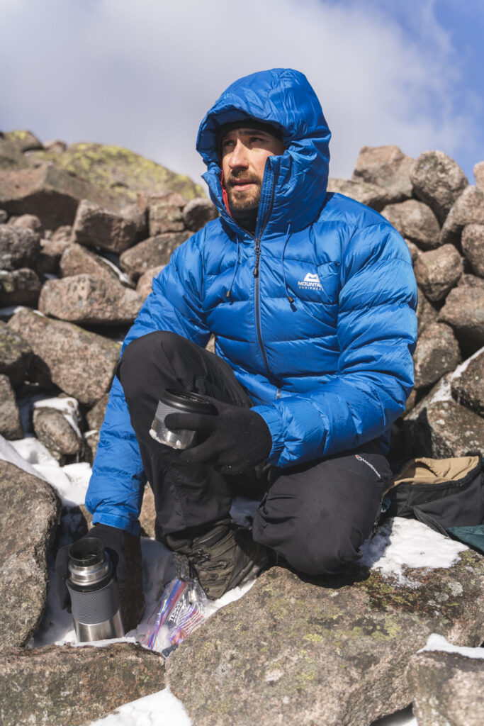 Adam Raja having a hot drink in the summit shelter of Càrn a’ Mhàim on a cold and windy morning in the Cairngorms.